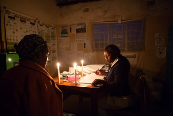 Two women sit in a dark room lit by candlelight