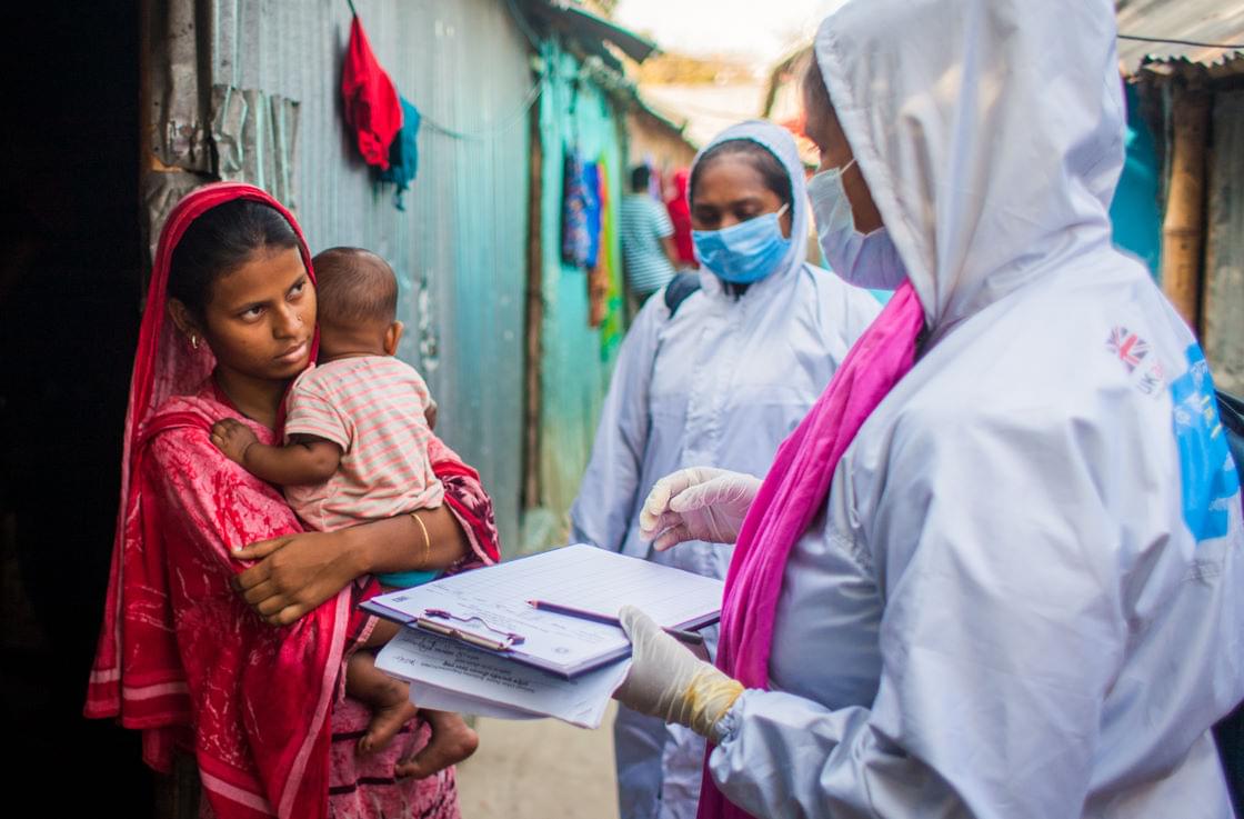 Community workers in protective suits talking to women in front of the dwelling